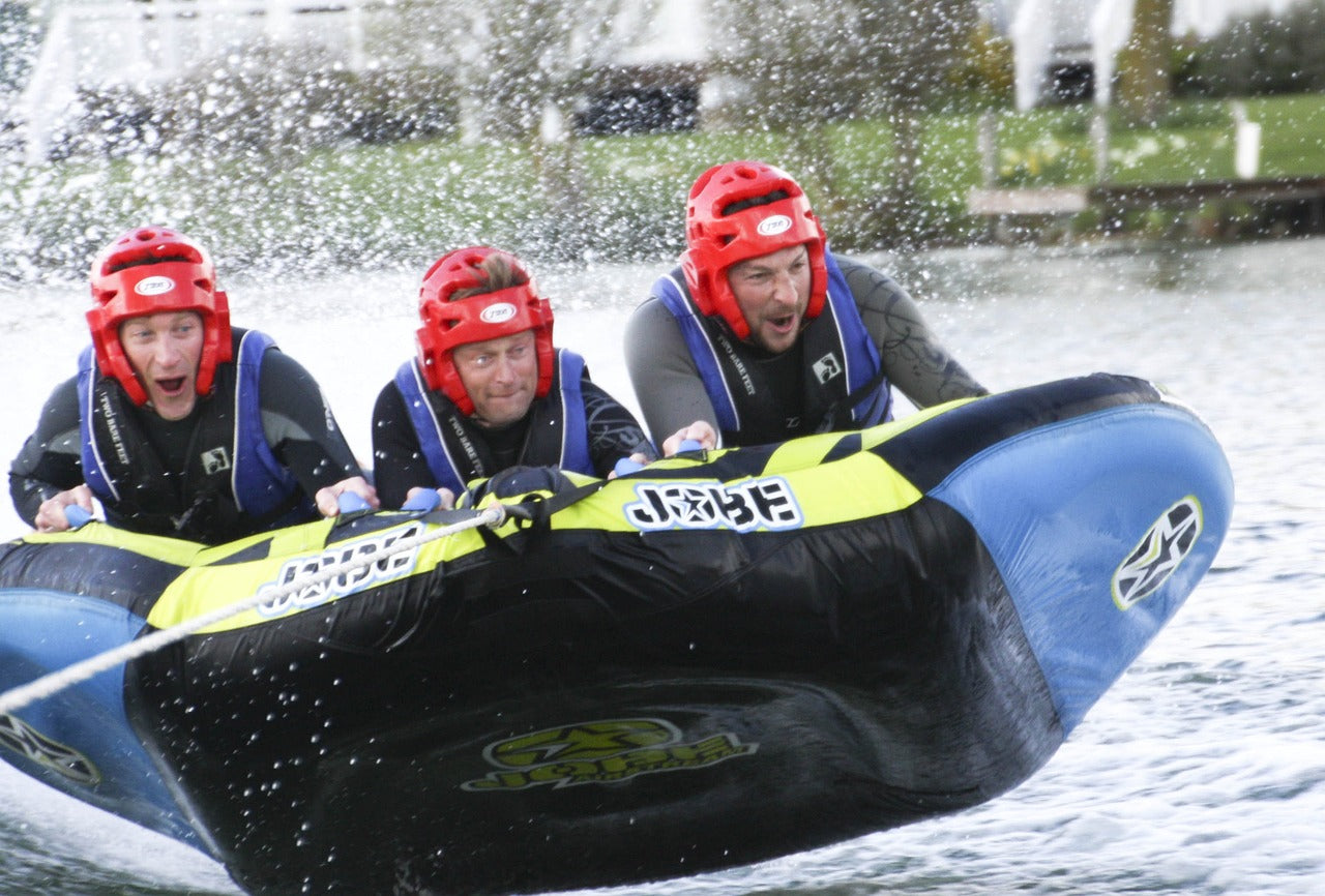 3 people in wetsuits and safety gear on a towed inflatable having fun 